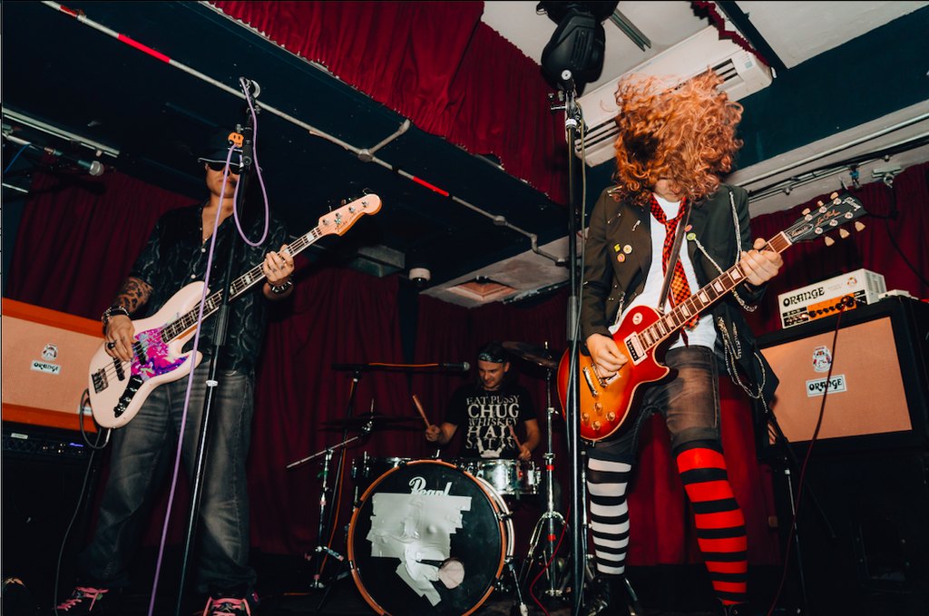Rat Hole playing live: a Ben the Dep on bass, Doctor Smackpot on drums, and Johnny Sideways mid headbang in red and white striped tights