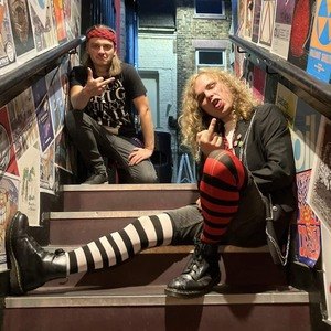 Doctor Smackpot (left) and Johnny Sideways (right) sitting on a stairwell covered in gig posters
